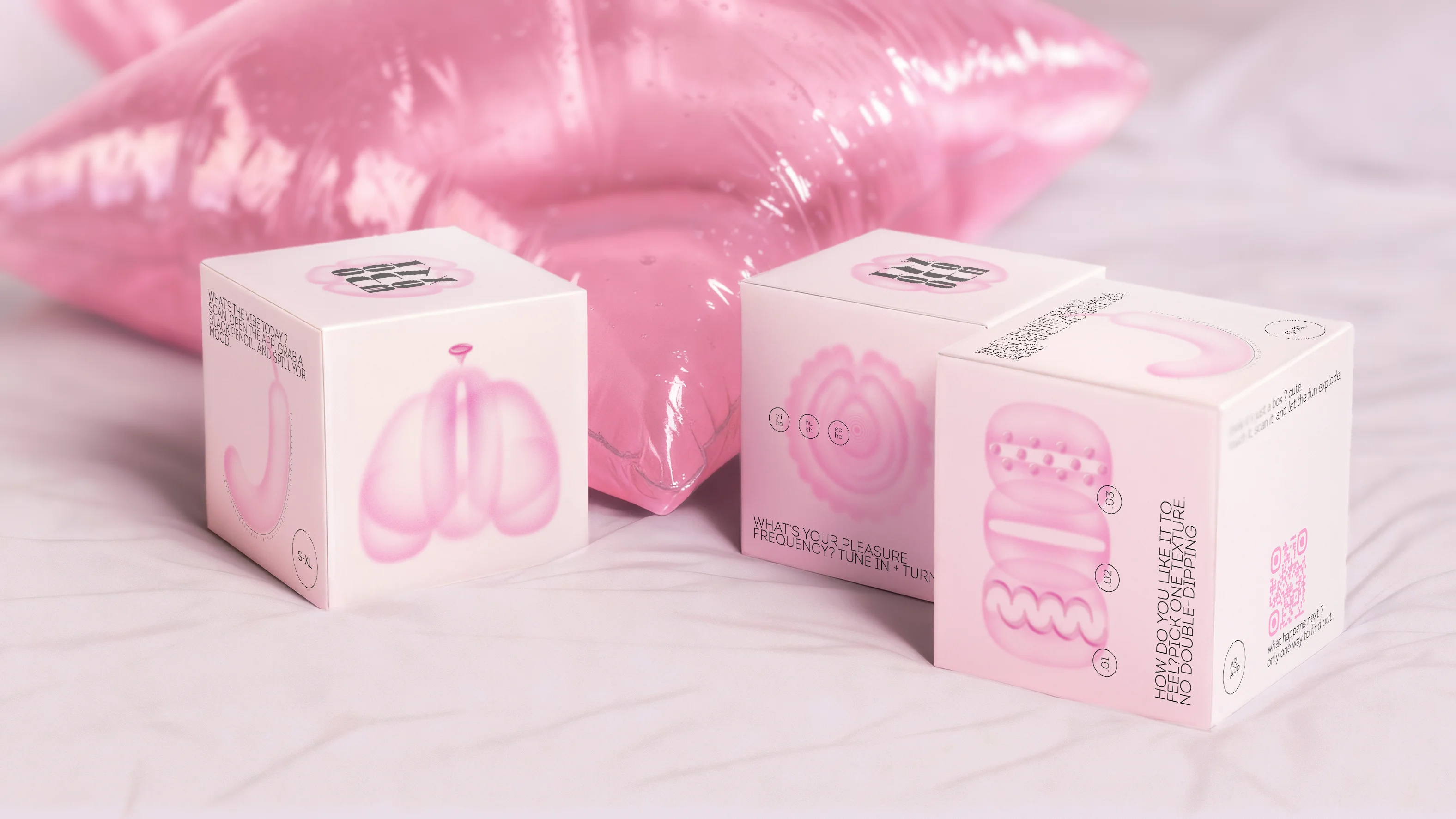 Three Oh My Box! interactive packaging cubes with soft pink illustrations and AR prompts, placed beside a shiny pink cushion.