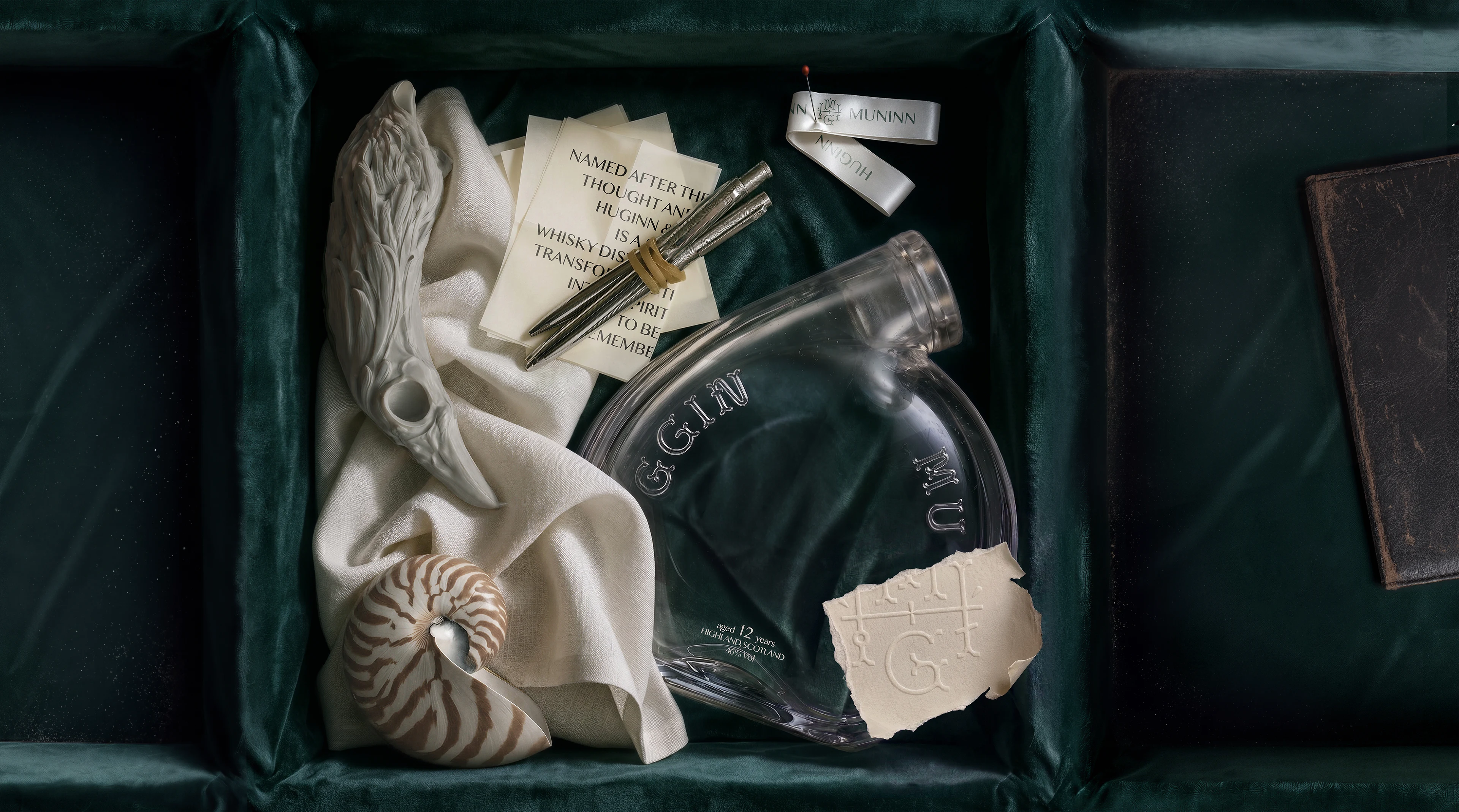Award-winning creative secondary packaging and bottle design for Huginn & Muninn whisky by DEEEZ Design & Creativity Ltd, featuring an empty custom glass bottle, sculpted raven closure, and tactile brand artifacts inside an emerald velvet collector’s casket.
